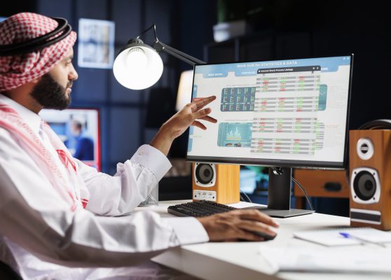An Arab businessman diligently analyzing data on his computer, making important decisions for the company. Muslim guy wearing traditional attire is checking charts and data on his desktop pc.